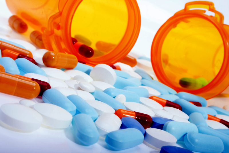 Im Hintergrund eine offene Medikamentendose und im Vordergrudn unsortierte Tabletten und Pillen, die analysiert werden müssen.