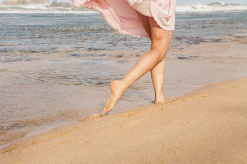 The young woman running on the beach barefoot